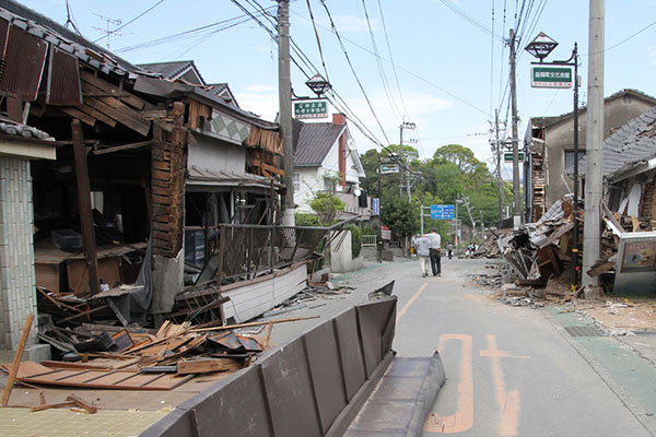 平成28年熊本地震で壊滅的な被害を受けた益城町の県道熊本高森線沿線の被害状況。倒壊した家屋の間を、肩を寄せ合って歩く老夫婦の写真。